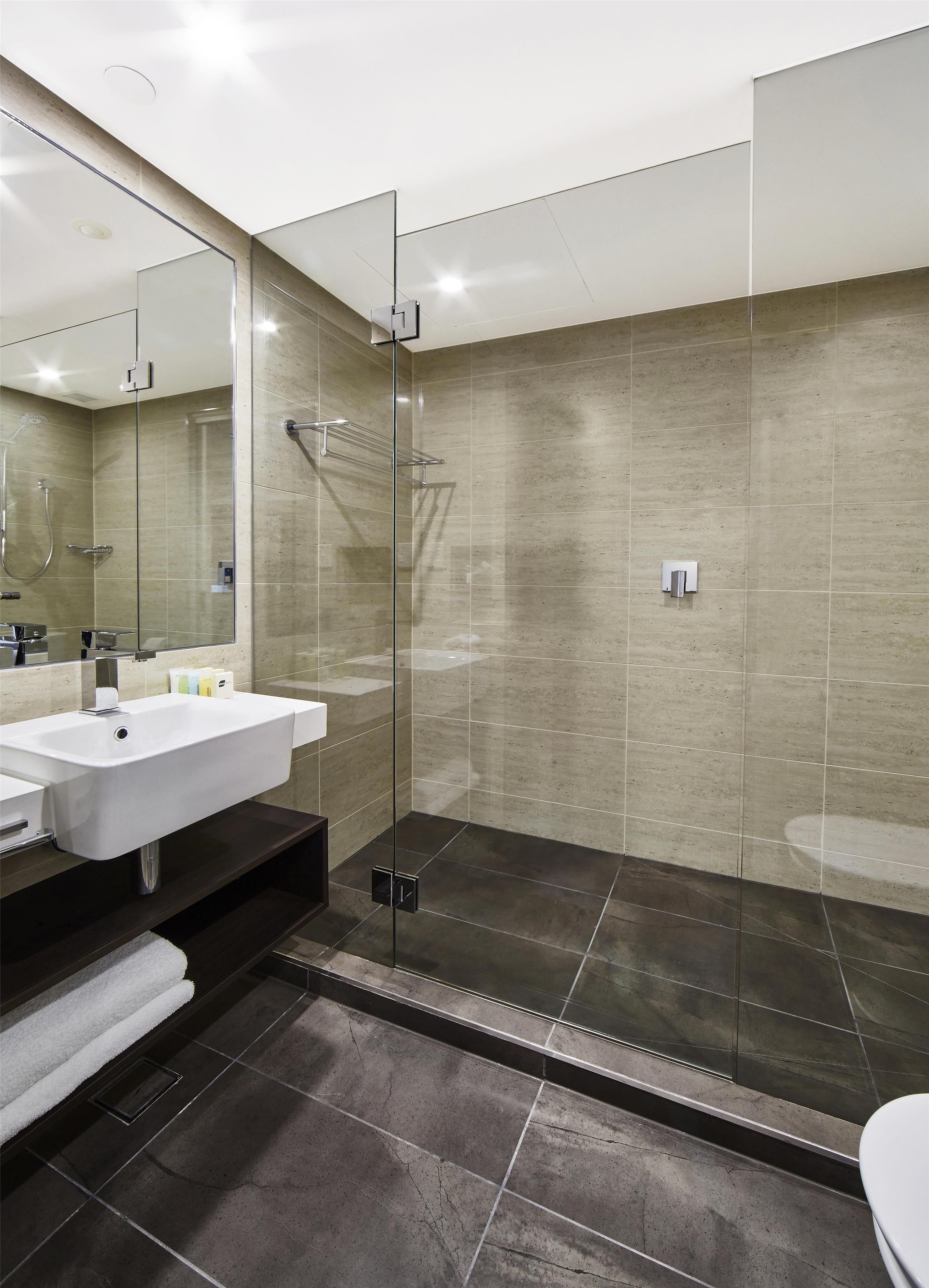 Un baño moderno con ducha de vidrio, un lavamanos blanco y suelo oscuro.