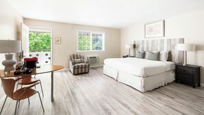 A hotel room with a bed, bedside tables, a desk with a chair, and a window with a view of greenery. - The Atlantic Hotel (Southampton)
