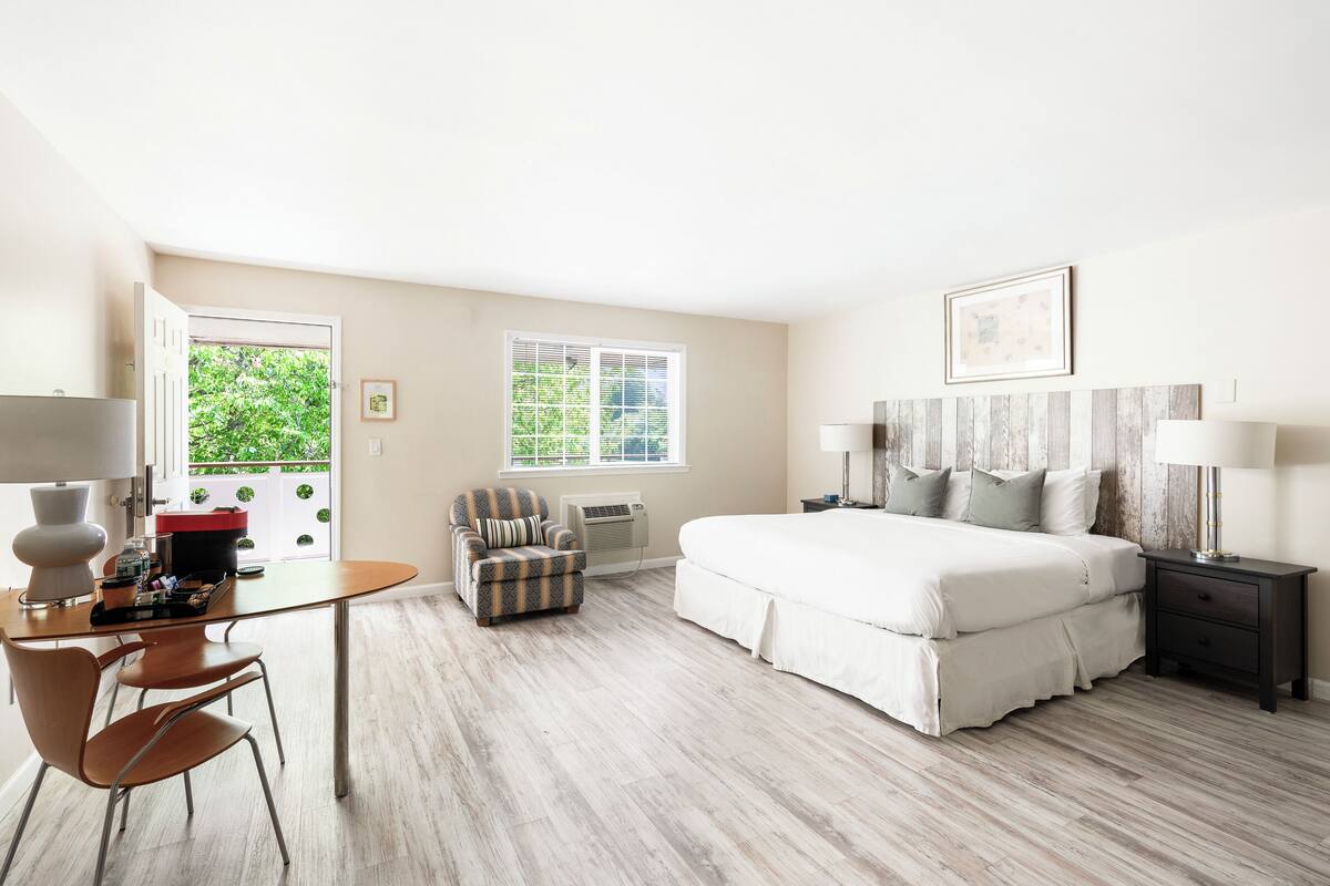 A hotel room with a bed, bedside tables, a desk with a chair, and a window with a view of greenery.