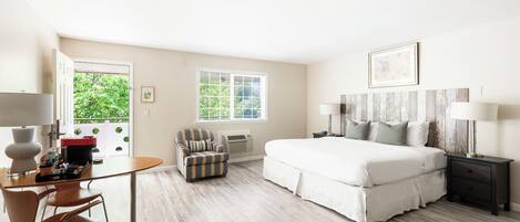 A hotel room with a bed, bedside tables, a desk with a chair, and a window with a view of greenery.