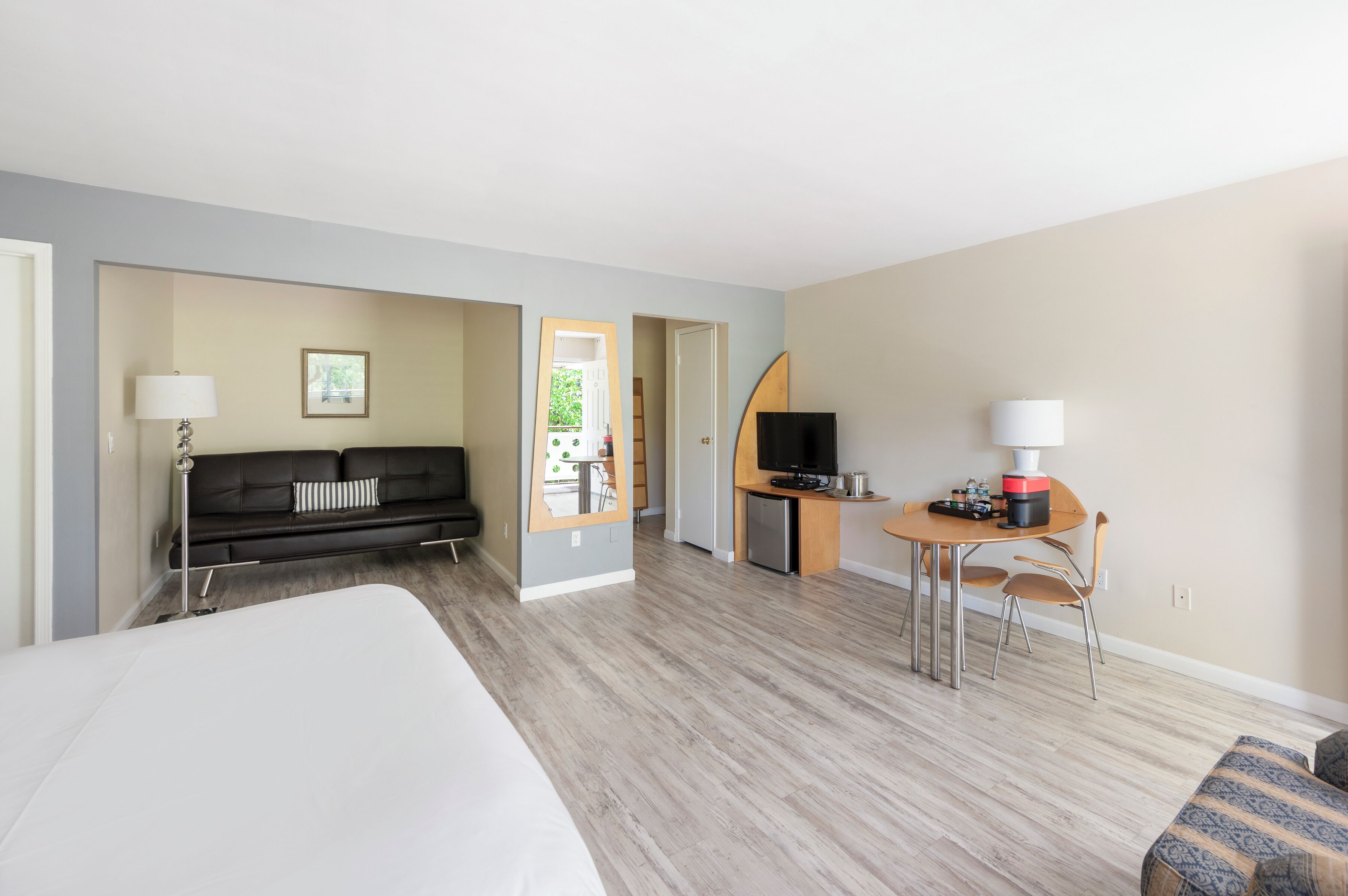 Habitación de hotel con cama, sofá, televisión, mesa de comedor y pequeña cocina.