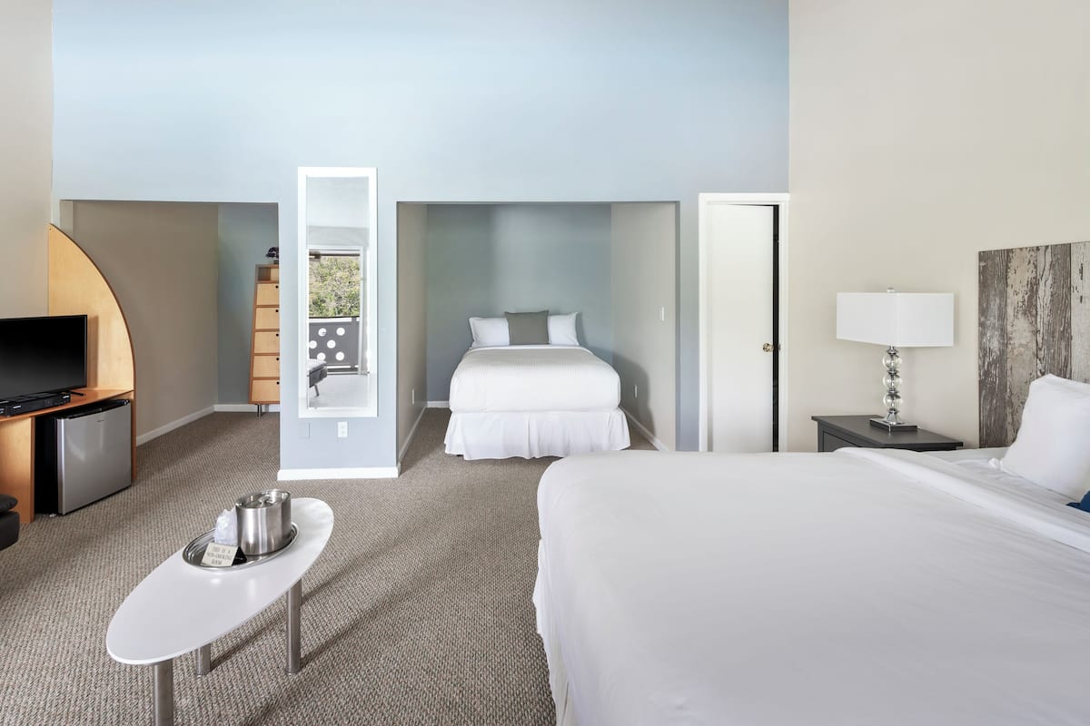 A hotel room with a bed, a TV, a small table with a tray, a door, and a view of the outside.