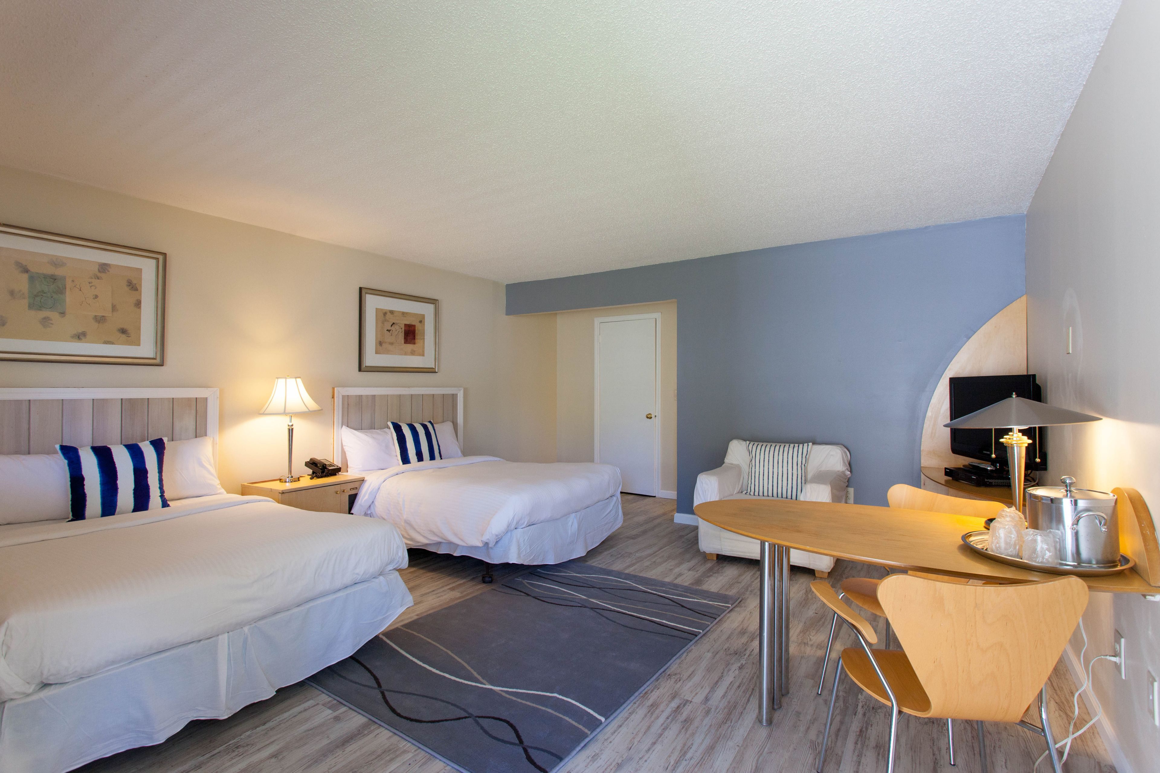 A hotel room with two beds, a dining table, a sofa, and a television.