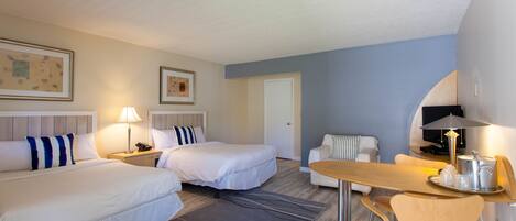 A hotel room with two beds, a dining table, a sofa, and a television.
