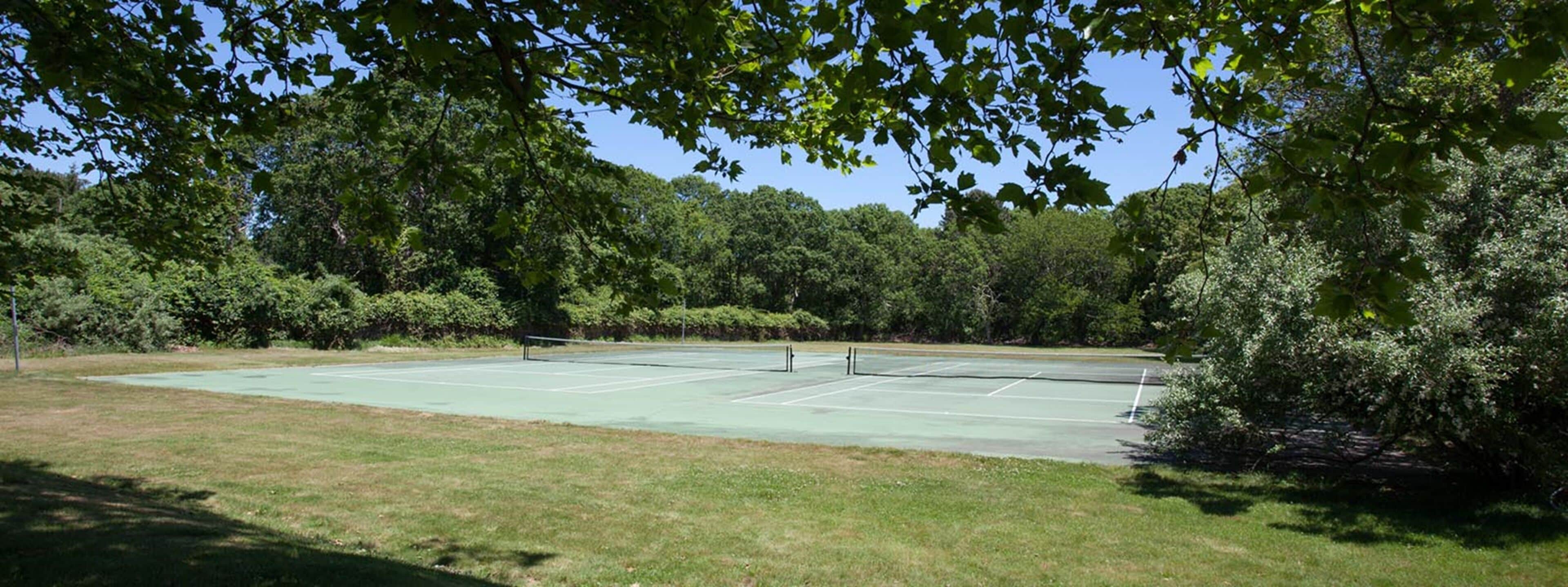 Una cancha de tenis al aire libre rodeada de árboles frondosos.