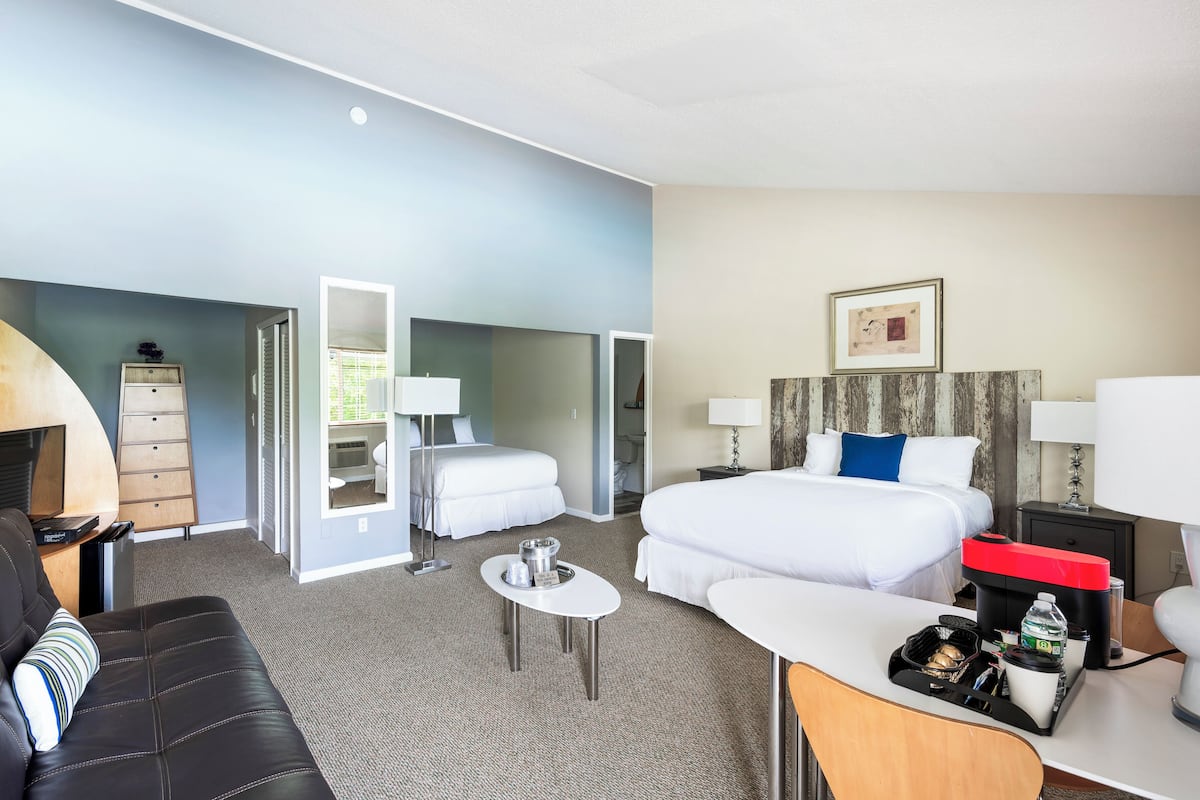 A hotel room with a bed, a desk, a chair, a sofa, and a small table with a tray.