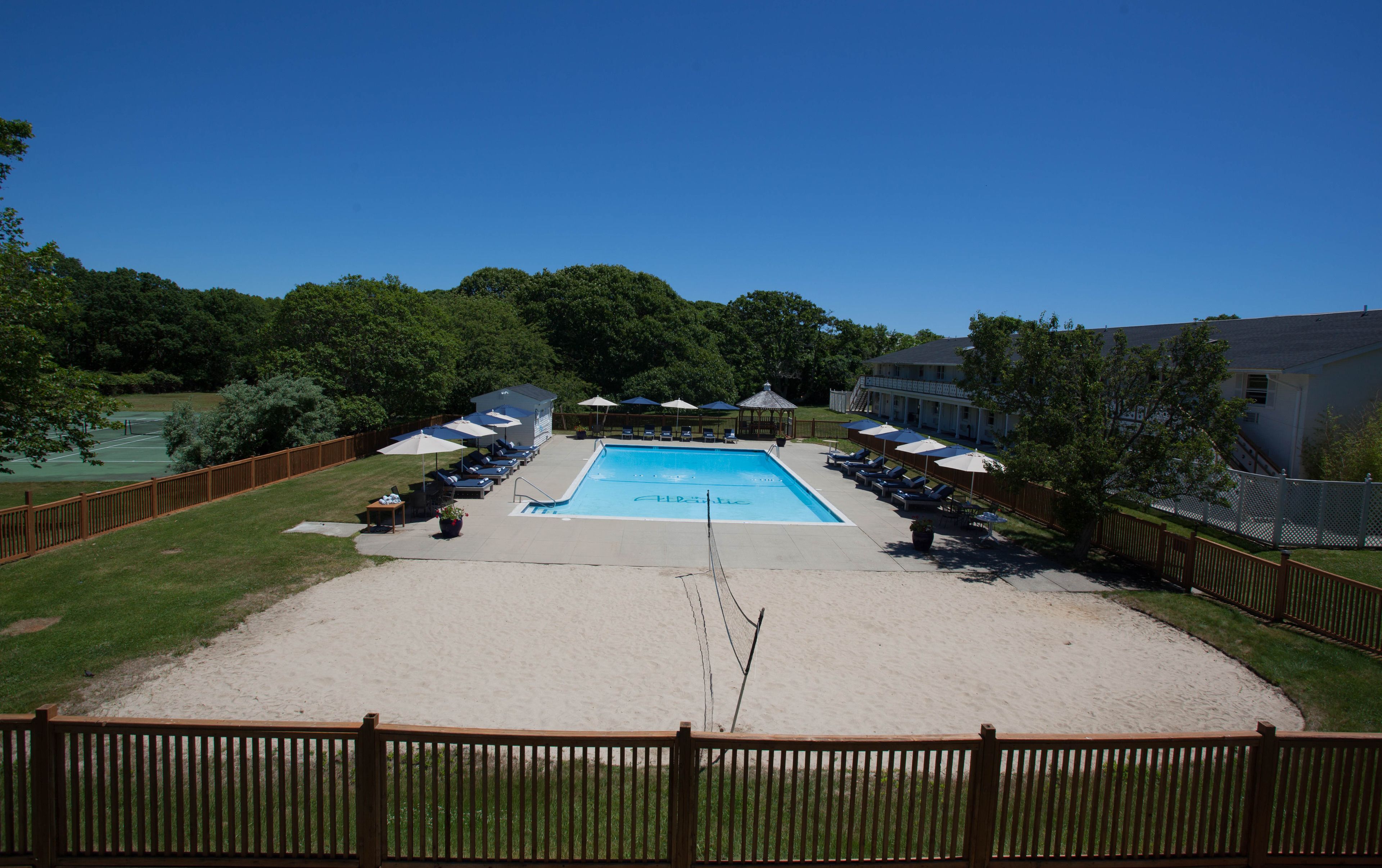 A swimming pool with lounge chairs and umbrellas, surrounded by a wooden fence and greenery.