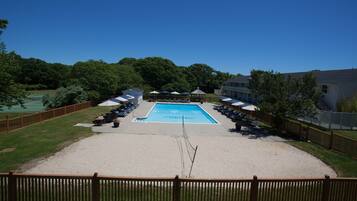A swimming pool with lounge chairs and umbrellas, surrounded by a wooden fence and greenery.