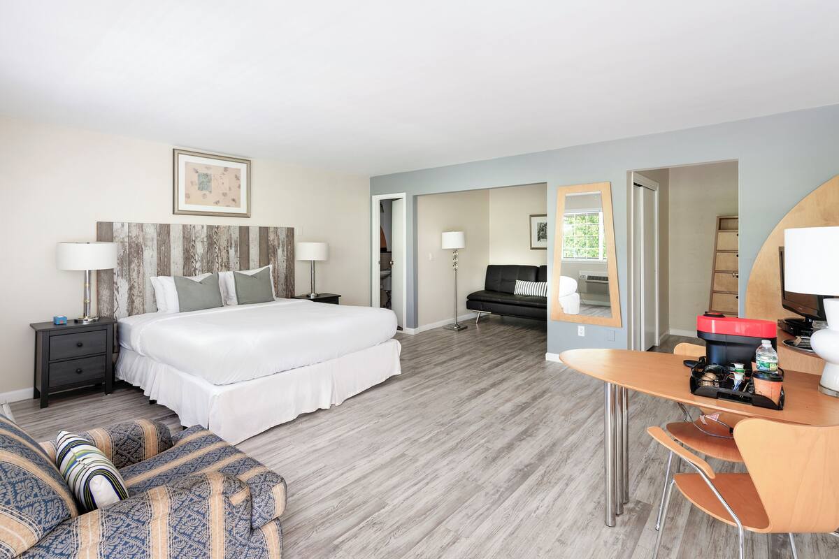 A modern hotel room with a large bed, bedside tables, a desk with a chair, a mirror, and a wardrobe.