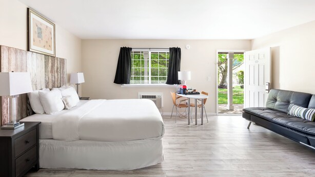 A hotel room with a bed, bedside tables, a desk with chairs, a sofa, a window with curtains, and a door leading outside. - The Atlantic Hotel (Southampton)