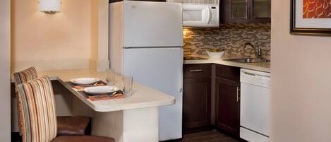 A compact kitchen with a refrigerator, microwave, and a small dining area with a bench and table.
