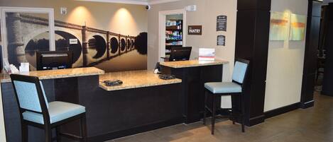 Un espace d’accueil comprenant un comptoir, deux tabourets de bar, un ordinateur et un écran fixé au mur.