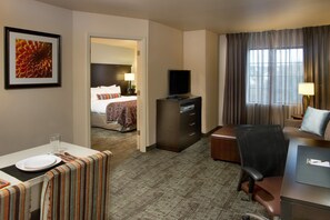 A hotel room with a bed, a desk with a laptop, a TV, and a dining area with a table set for two. - Staybridge Suites Myrtle Beach - West by IHG (Myrtle Beach)