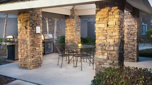 An outdoor patio with stone pillars, a grill, and a table with chairs. - Staybridge Suites Myrtle Beach - West by IHG (Myrtle Beach)