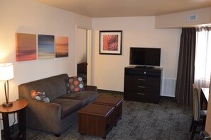 Una sala de estar con un sofá, otomanas, un televisor, una lámpara y obras de arte en la pared.