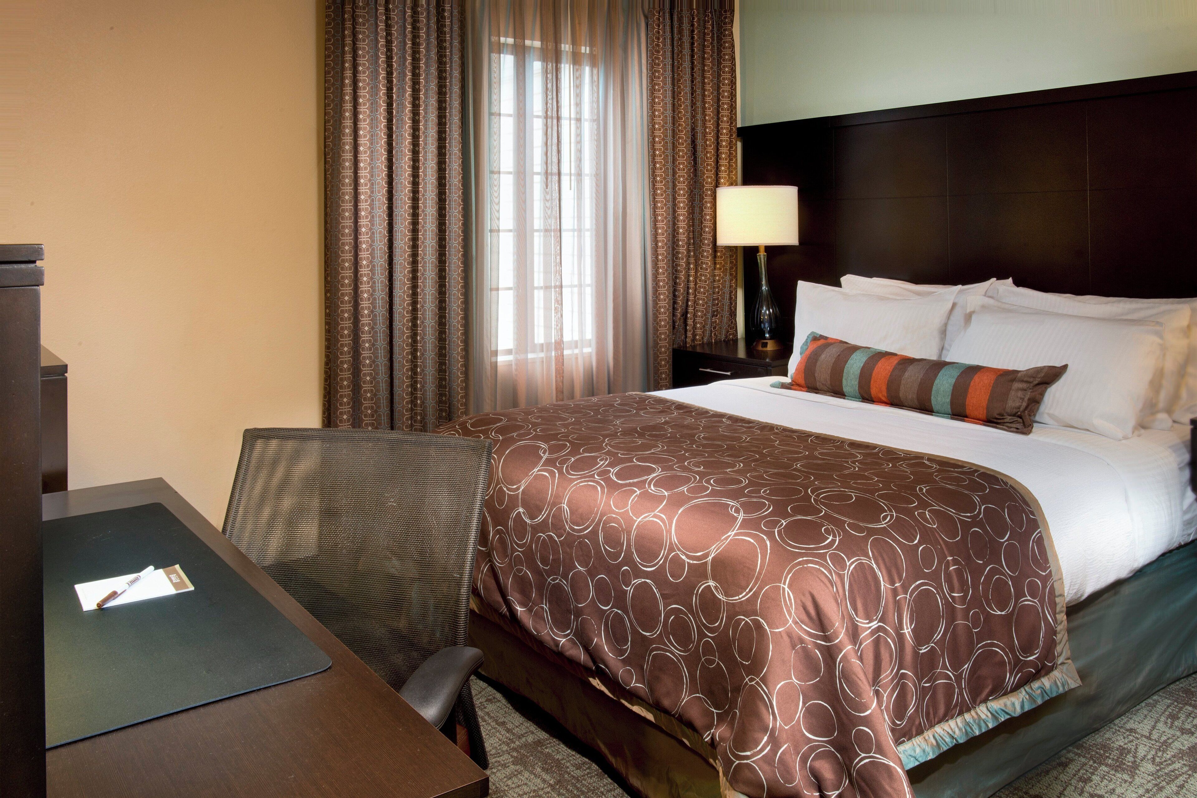 A hotel room with a bed, a desk, a chair, and a lamp.