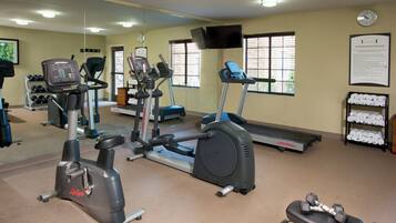 A gym with various exercise equipment, a clock, and a sign with rules.