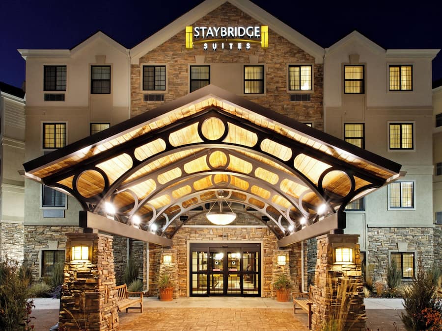 A Staybridge Suites hotel with a stone facade, a covered entrance with circular skylights, and a well-lit front door.