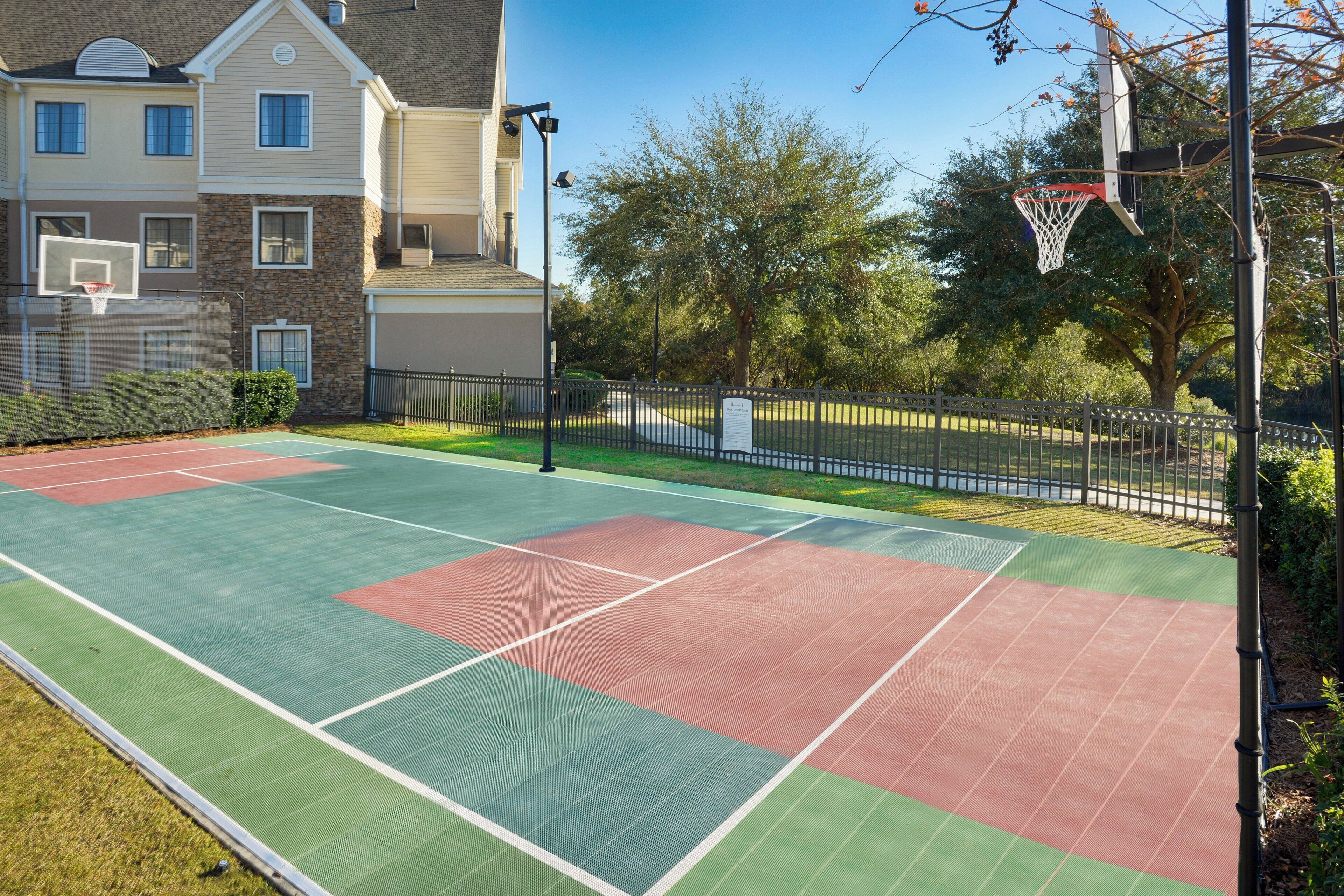 Ein Basketballplatz im Freien neben einem Wohngebäude mit einem eingezäunten Bereich und Bäumen.