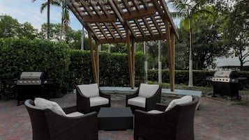 Un patio al aire libre con mobiliario de mimbre, una pérgola y dos parrillas para barbacoa.