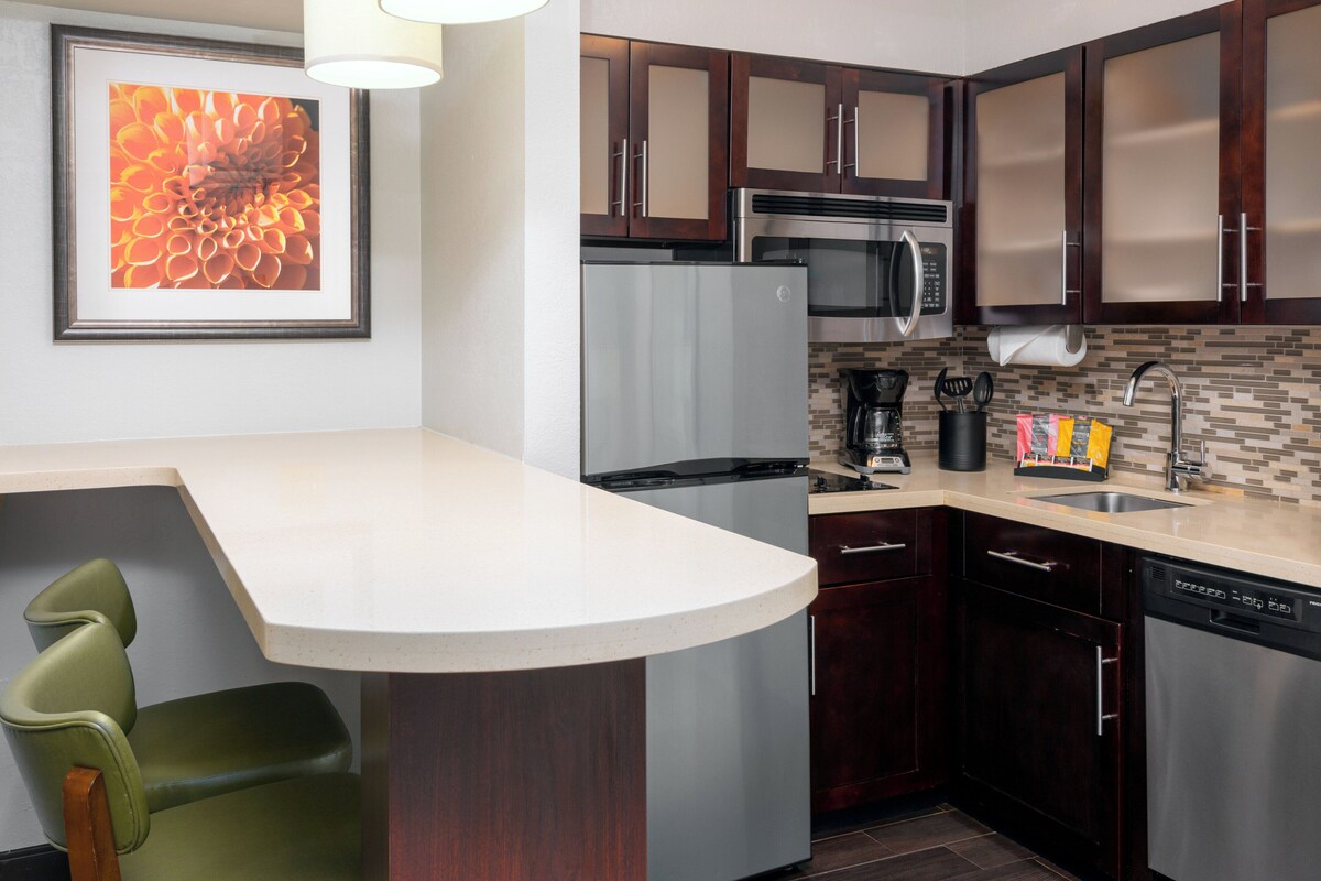 A modern kitchen with a curved island, stainless steel appliances, dark wooden cabinets, and a tiled backsplash.