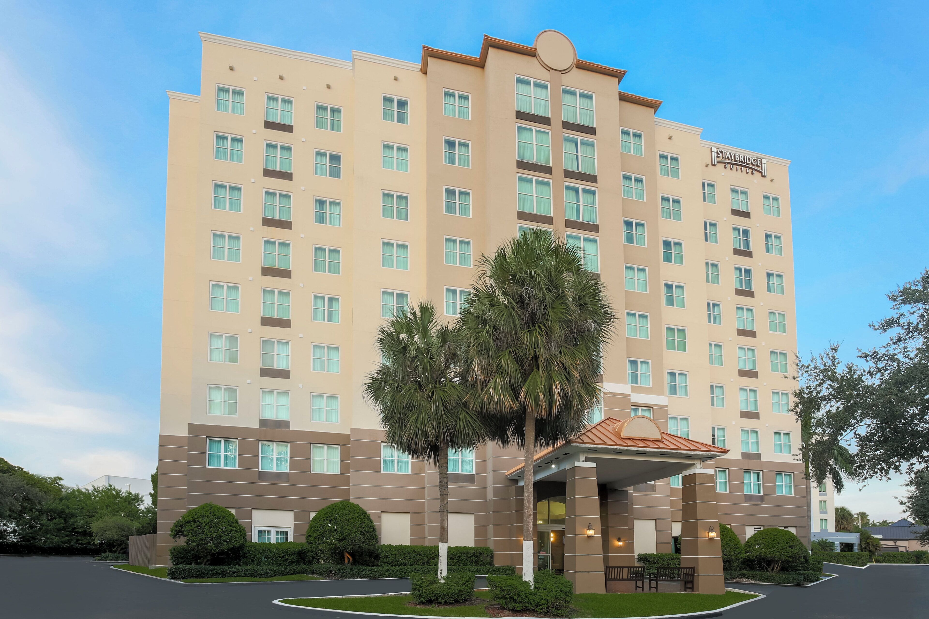 A multi-story hotel with a central entrance, a parking lot, and surrounding greenery.