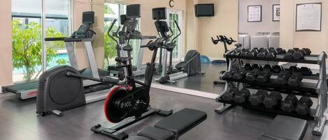 Un gimnasio con máquinas de cardio, mancuernas y bancos.
