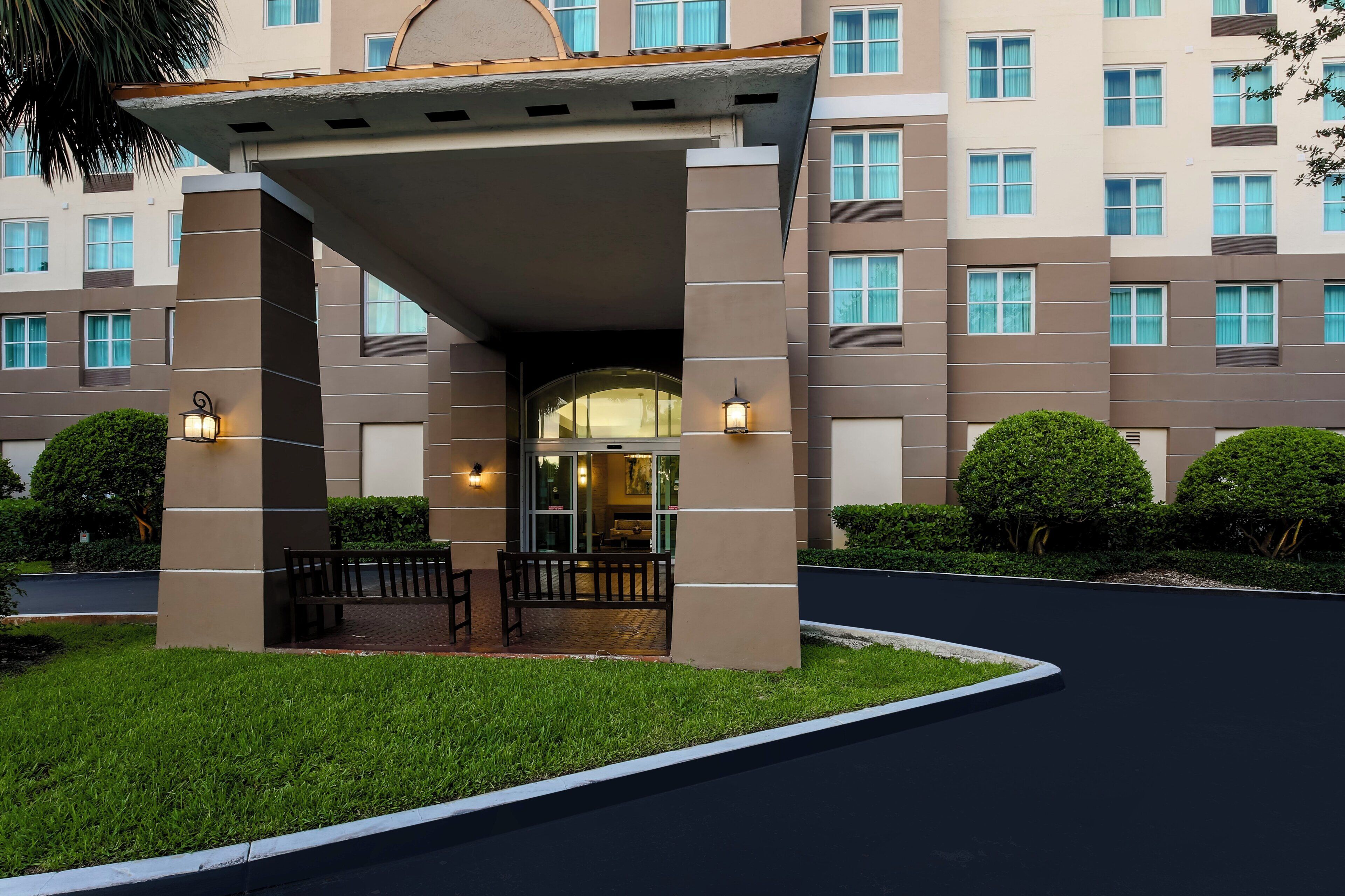 A hotel entrance with a covered waiting area, a reception desk, and a parking lot.