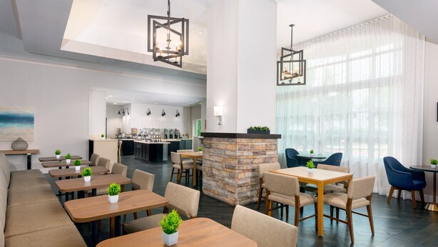 A modern restaurant with wooden tables and chairs, a stone fireplace, and large windows with sheer curtains. - Staybridge Suites Miami Doral Area by IHG (Miami)