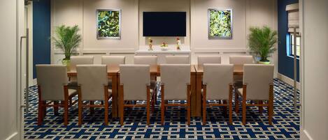 A conference room with a large table and chairs, a flat-screen TV, and two potted plants.