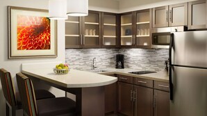 A modern kitchen with dark wooden cabinets, a stainless steel refrigerator, a coffee maker, and a bowl of fruit on the counter.