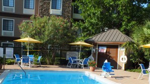 A swimming pool with blue water, surrounded by blue chairs and yellow umbrellas. There are signs indicating no lifeguard on duty. - Staybridge Suites Irving Las Colinas by IHG (Irving)