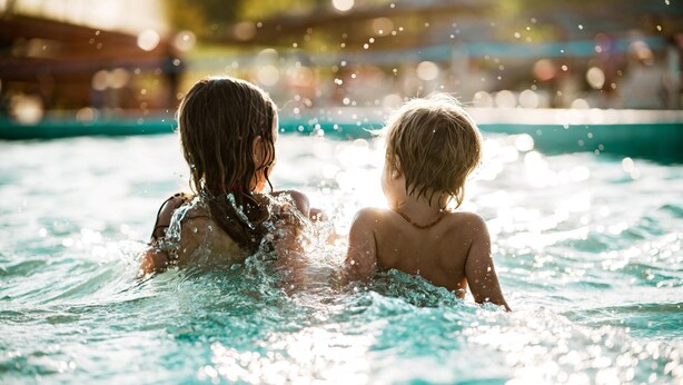 Two children in a swimming pool with water splashing around them.