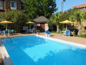 A swimming pool with lounge chairs and umbrellas, surrounded by trees and a building with a sign indicating no lifeguard on duty. - Staybridge Suites Irving Las Colinas by IHG (Irving)