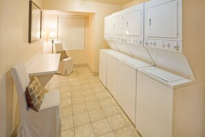 A laundry room with a table, chairs, and a row of stacked washers and dryers. - Staybridge Suites Irving Las Colinas by IHG (Irving)
