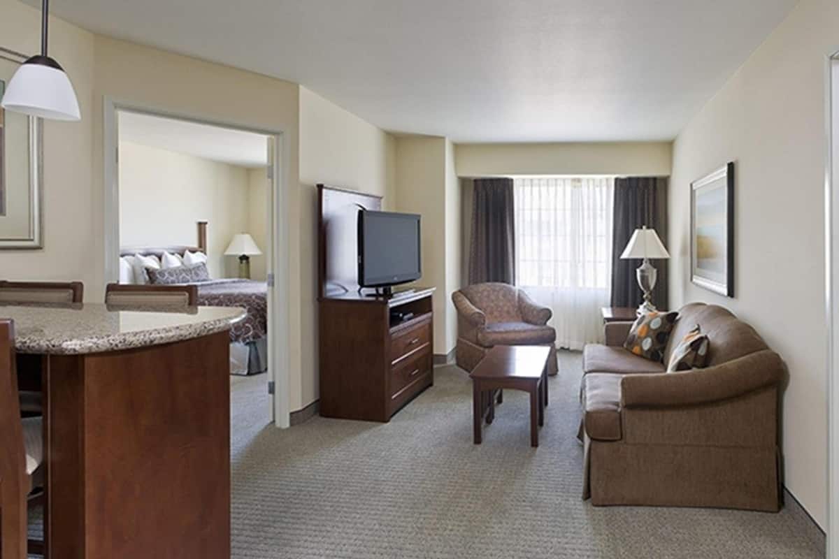 A hotel room with a kitchenette, a television, a sofa, a chair, and a bed.