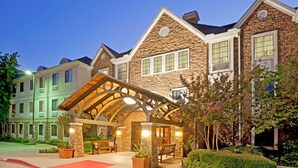 A hotel with a stone facade, a covered entrance, and a landscaped garden. - Staybridge Suites Irving Las Colinas by IHG (Irving)