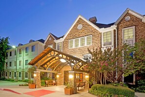 A hotel with a stone facade, a covered entrance, and a landscaped garden. - Staybridge Suites Irving Las Colinas by IHG (Irving)