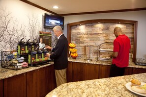 A breakfast bar with coffee machines, a fruit display, and a television mounted on the wall. - Staybridge Suites Irving Las Colinas by IHG (Irving)