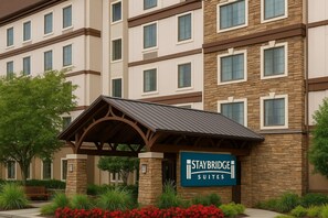 A Staybridge Suites hotel with a stone facade, multiple windows, and a covered entrance. - Staybridge Suites Irving Las Colinas by IHG (Irving)