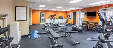 A gym with exercise equipment, a treadmill, weights, and a wall-mounted TV.