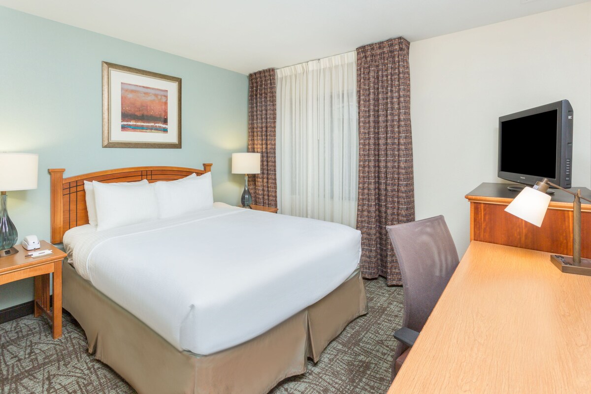 A hotel room with a large bed, a desk with a computer, a television, and a framed picture on the wall.