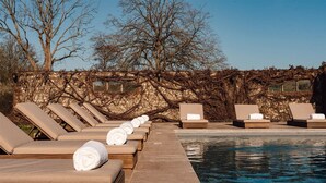 Zona de piscina con sillones de descanso y toallas, rodeada por un muro de piedra cubierto de hiedra.