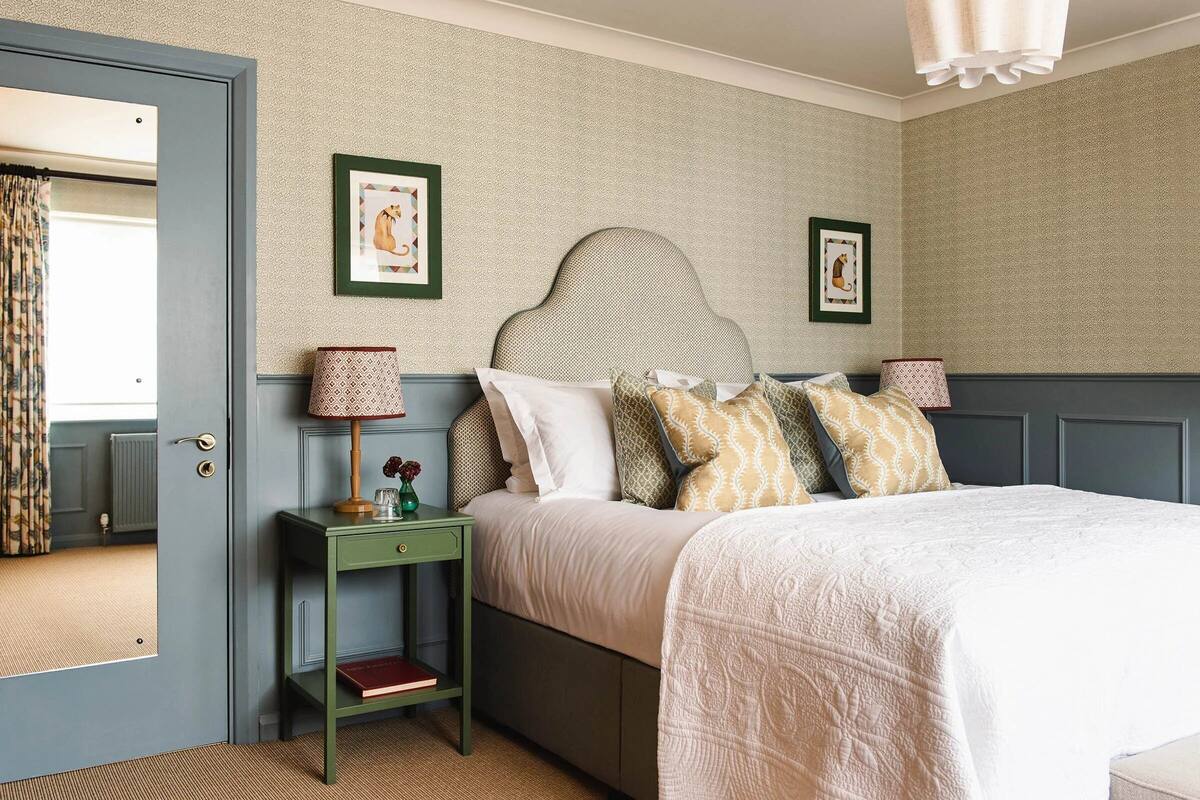 A bedroom with a bed, a nightstand, a mirror, and two framed pictures on the wall.