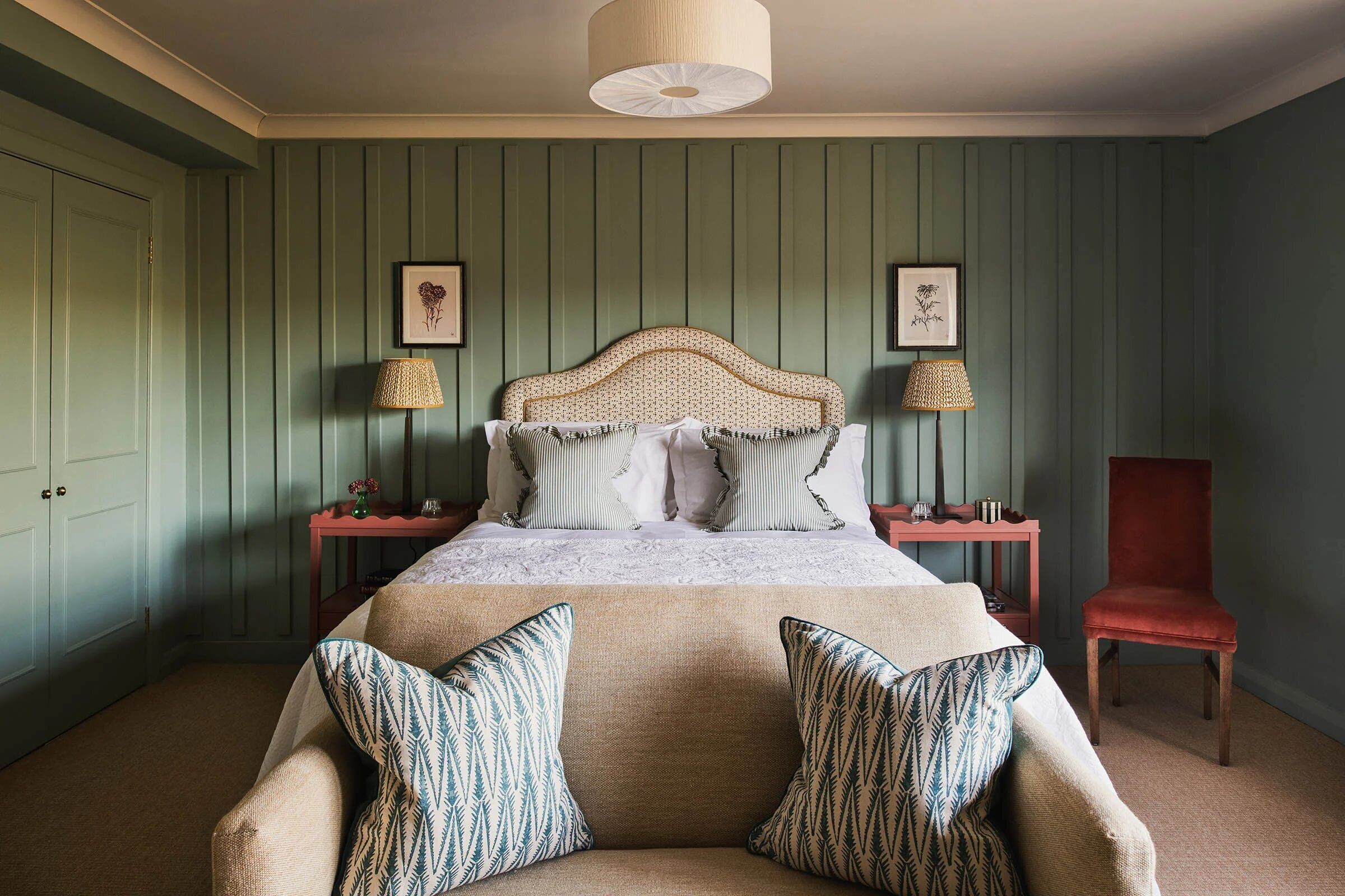 A bedroom with a bed, two nightstands, a red chair, and a green wall.