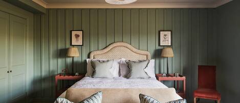 A bedroom with a bed, two nightstands, a red chair, and a green wall.
