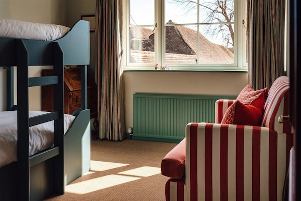 Una habitación con literas, un radiador, una ventana con cortinas y un sillón a rayas.