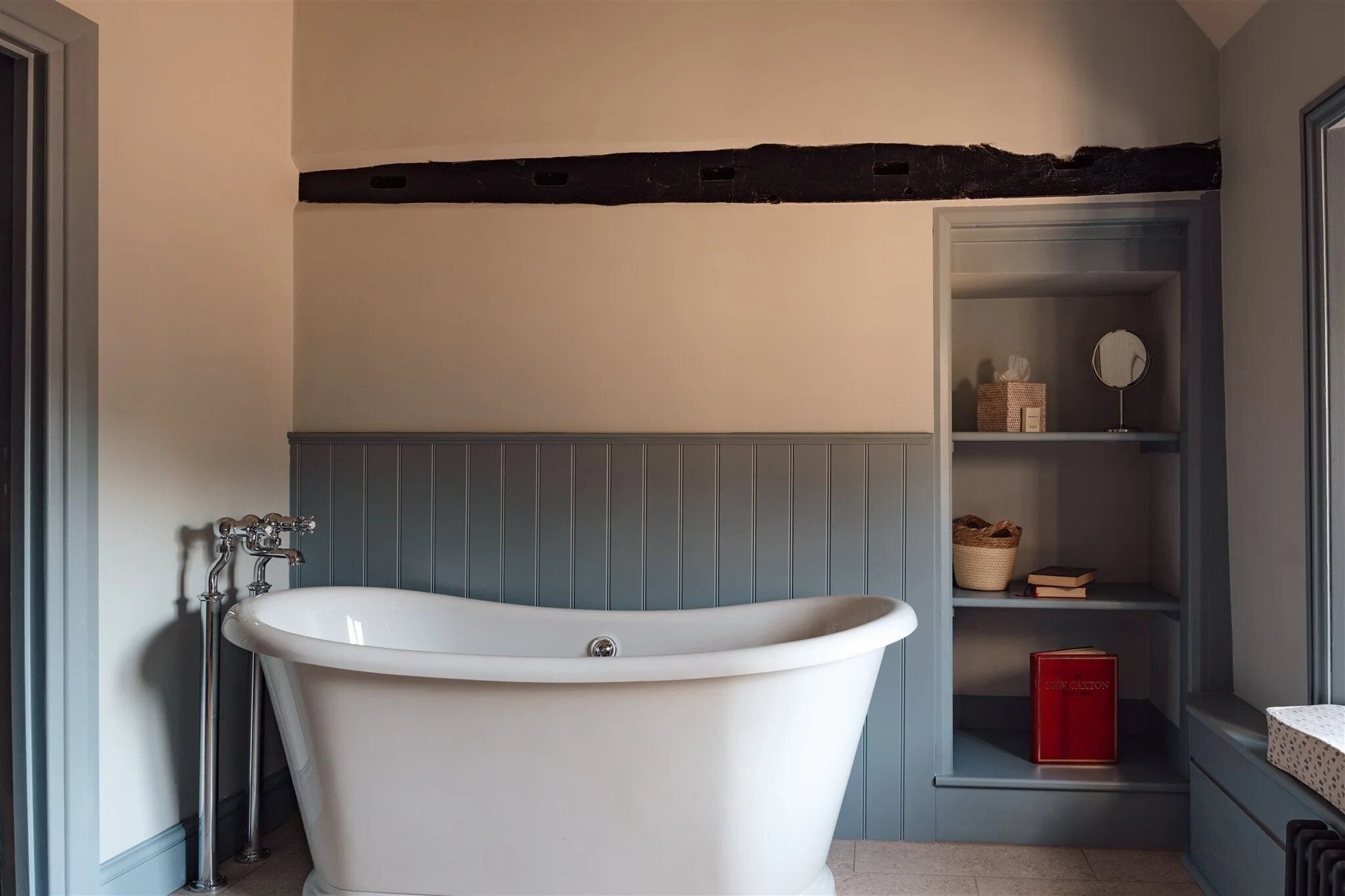 A bathroom with a freestanding bathtub, a shelf with a basket and books, and a mirror.
