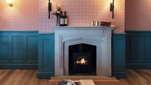 Una habitación acogedora con chimenea, papel tapiz estampado y un banco con revistas.