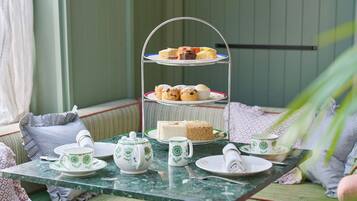 A three-tiered tea service stand with sandwiches and cakes, surrounded by tea cups and saucers on a table.